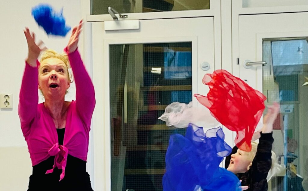 Peuters aan het dansen met de juf en met rood wit blauwe sjalen